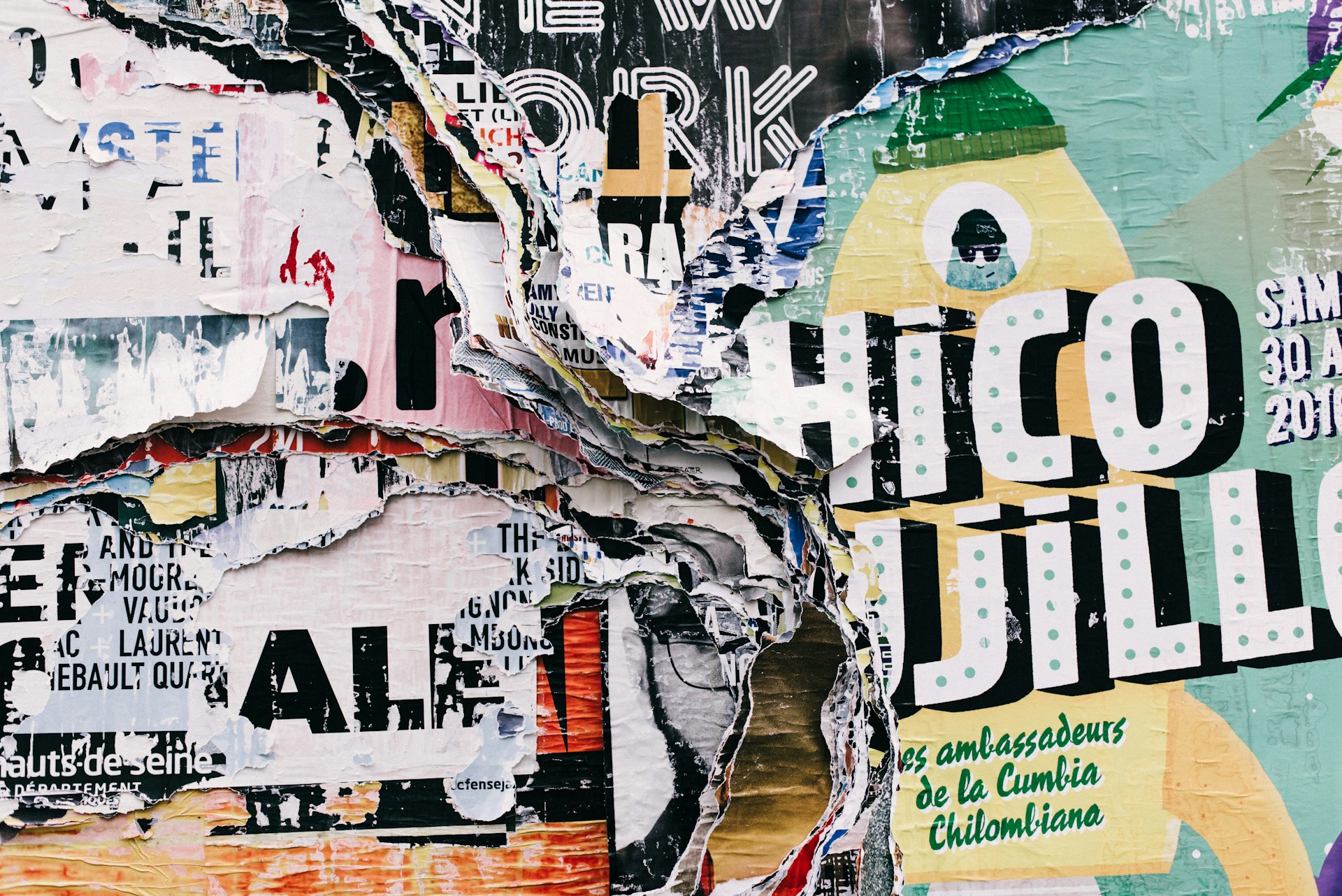 A vibrant collage of heavily layered, torn street posters and textured billboard advertisements with bold typography.