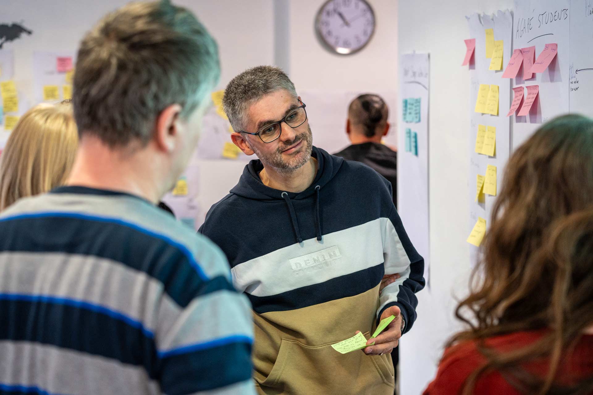 Participants collaborate during a NextSteps digital strategies training, featuring a man with glasses holding a sticky note while listening to a group discussion next to a whiteboard.