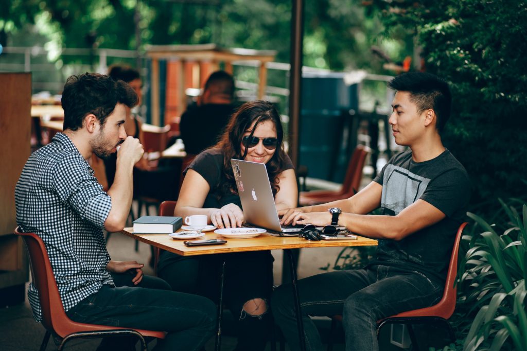 Two guys and girl sit at table looking at laptop