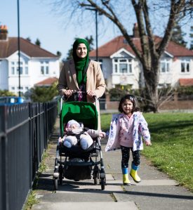 British Asian mother and young children enjoying exercise Full length front view of early 30s mother, 2 year old daughter, and 5 month old son in stroller approaching camera on late winter walk in West London suburb.